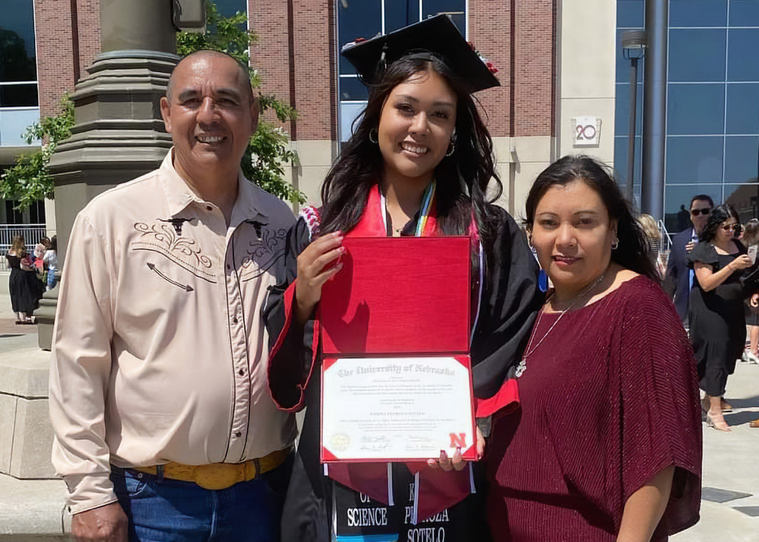 Student standing with her parents while holding her diploma